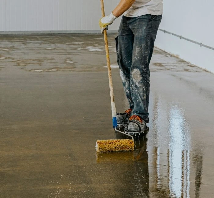 Worker applying epoxy flooring with a roller during the installation process in a commercial space.