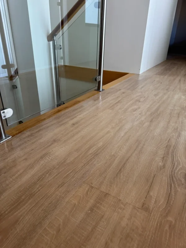 Light hybrid flooring in a modern hallway next to a glass balustrade and timber handrail